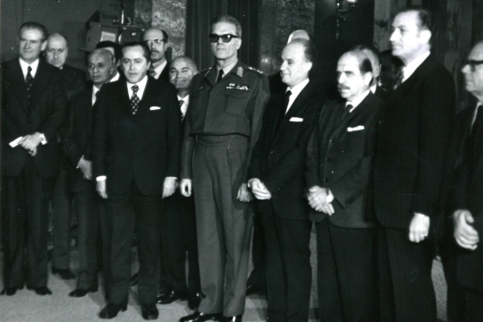 Το πρώτο κλιμάκιο του υπουργικού συμβουλίου της χούντας Ιωαννίδη (26/11/1973). Στη μέση, ένστολος ο «Πρόεδρος της Δημοκρατίας» Φίδων Γκιζίκης, στα αριστερά του ο «πρωθυπουργός» Αδαμάντιος Ανδρουτσόπουλος
